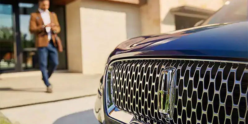 Close-up of a luxury car grille with a man walking in the background.