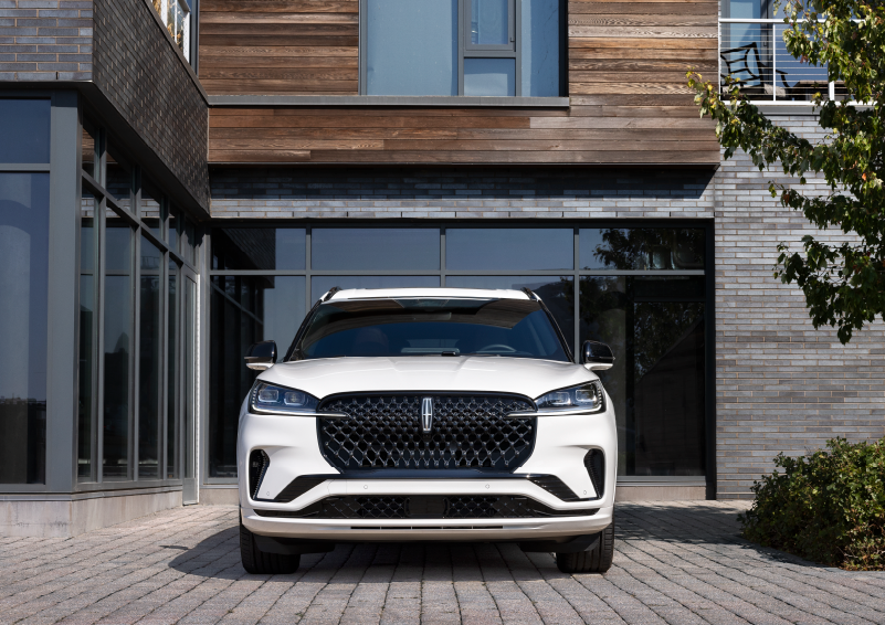 A white 2025 Lincoln Aviator® SUV is shown parked outside a modern building with gray brick and wood accents. | Lincoln of Ramsey in Ramsey NJ
