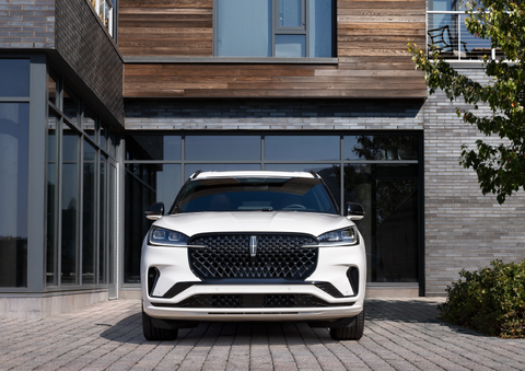 A white 2025 Lincoln Aviator® SUV is shown parked outside a modern building with gray brick and wood accents. | Lincoln of Ramsey in Ramsey NJ