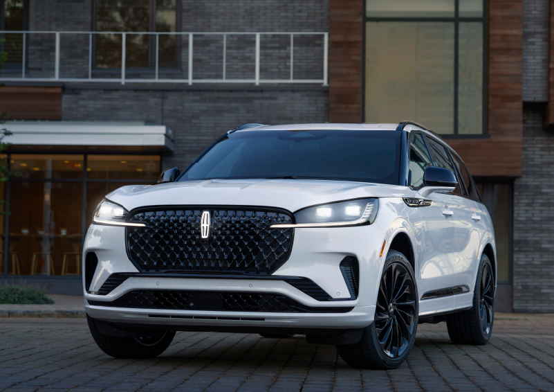 A white 2025 Lincoln Aviator® SUV is shown parked outside a modern building with gray brick and wood accents. | Lincoln of Ramsey in Ramsey NJ