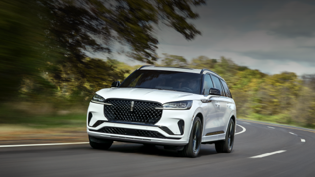A white 2025 Lincoln Aviator® SUV is being driven down a road lined with trees. | Lincoln of Ramsey in Ramsey NJ
