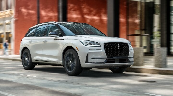 A white 2025 Lincoln Corsair® SUV with the Jet Appearance Package is being driven through a city.| Lincoln of Ramsey in Ramsey NJ