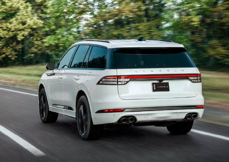 A white 2026 Lincoln Aviator® SUV is being driven away down a road lined with colorful trees. | Lincoln of Ramsey in Ramsey NJ