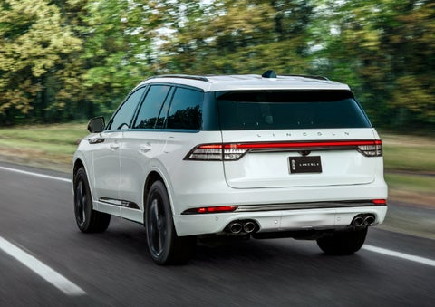 A white 2026 Lincoln Aviator® SUV is being driven away down a road lined with colorful trees. | Lincoln of Ramsey in Ramsey NJ