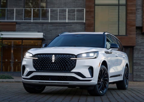 A 2026 Lincoln Aviator® Reserve model is shown with the available Jet Appearance Package parked near a restaurant. | Lincoln of Ramsey in Ramsey NJ
