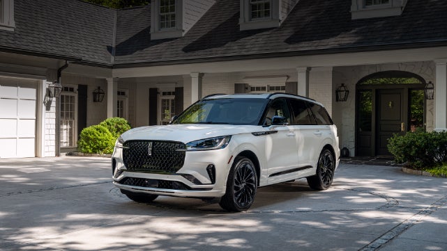 A white 2026 Lincoln Aviator® SUV is parked in the driveway of a luxury home. | Lincoln of Ramsey in Ramsey NJ