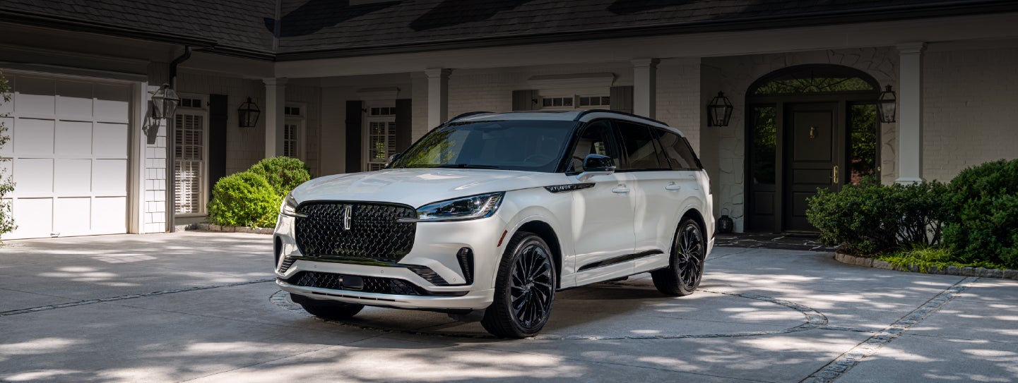 A white 2026 Lincoln Aviator® SUV is parked in the driveway of a luxury home. | Lincoln of Ramsey in Ramsey NJ