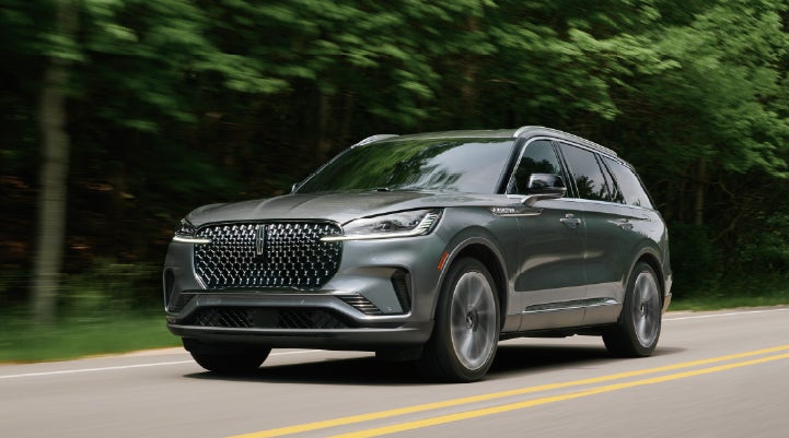 A 2027 Lincoln Aviator® SUV is being driven down a road lined with trees. | Lincoln of Ramsey in Ramsey NJ