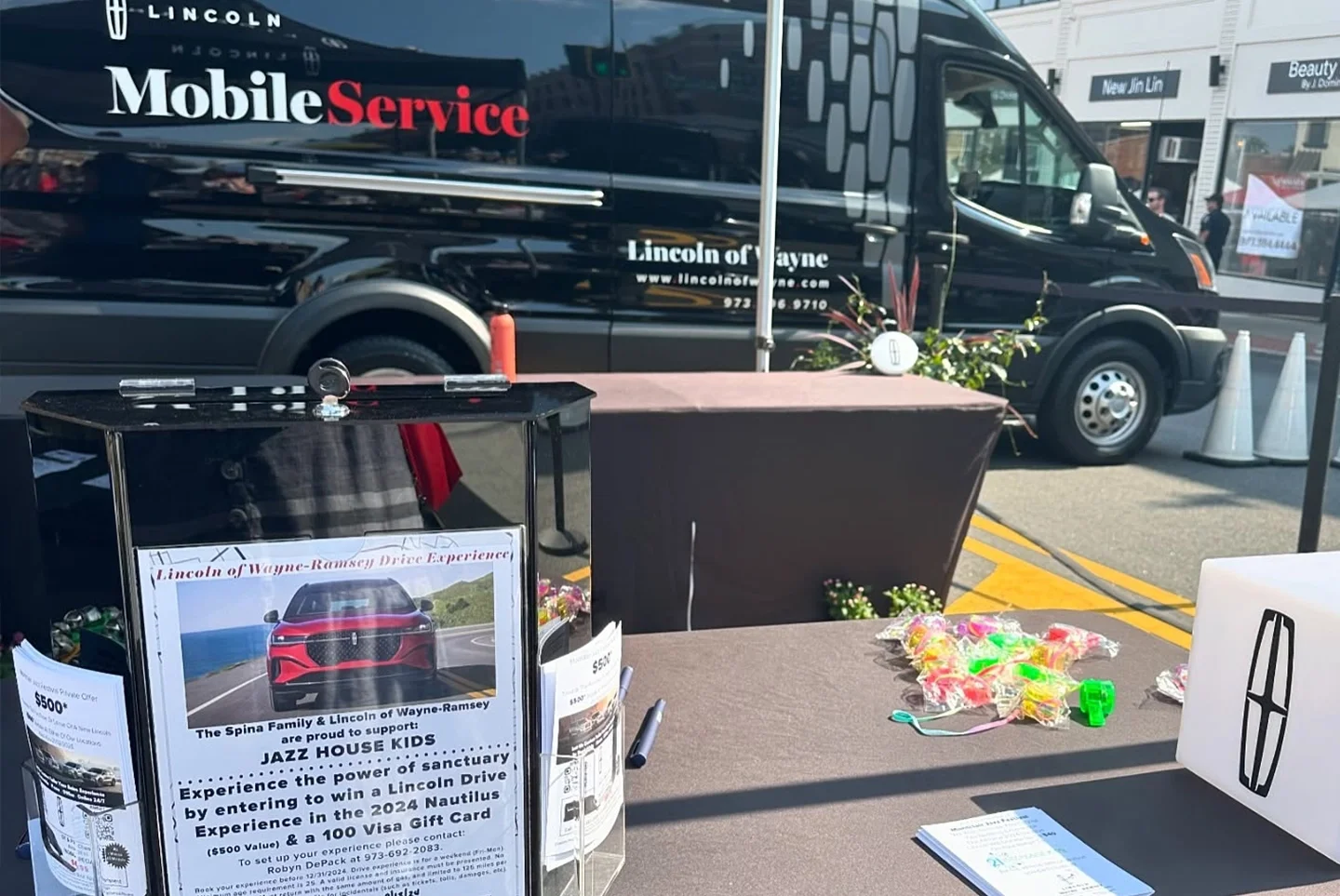 A black Lincoln Mobile Service van is parked behind a promotional display with a raffle for a car and gift card.
